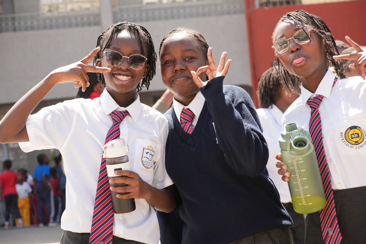 Three Junior Secondary girls waving in the school yard