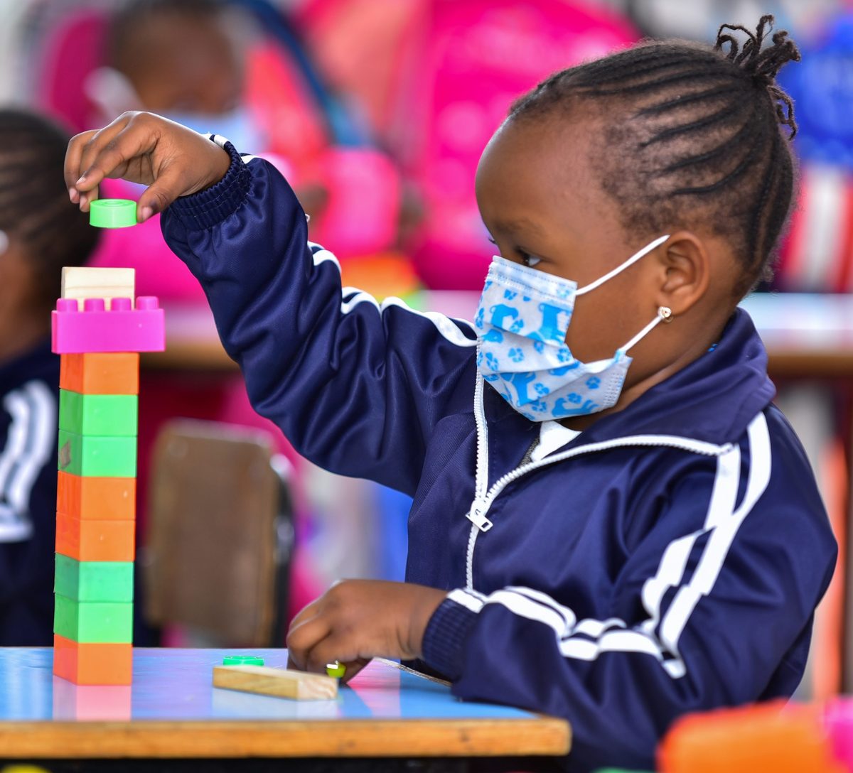 A kindergarten girl in a navy tracksuit balancing a block on top of a tall tower