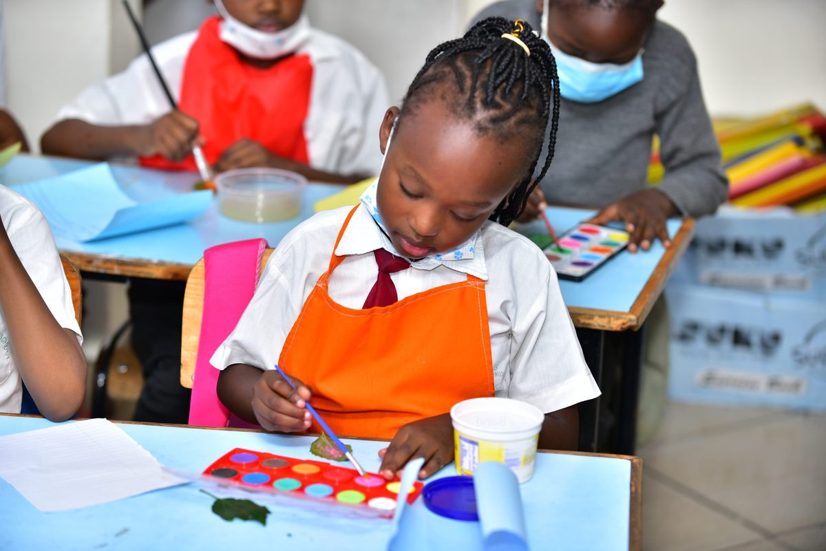 A girl in an orange apron painting with watercolours