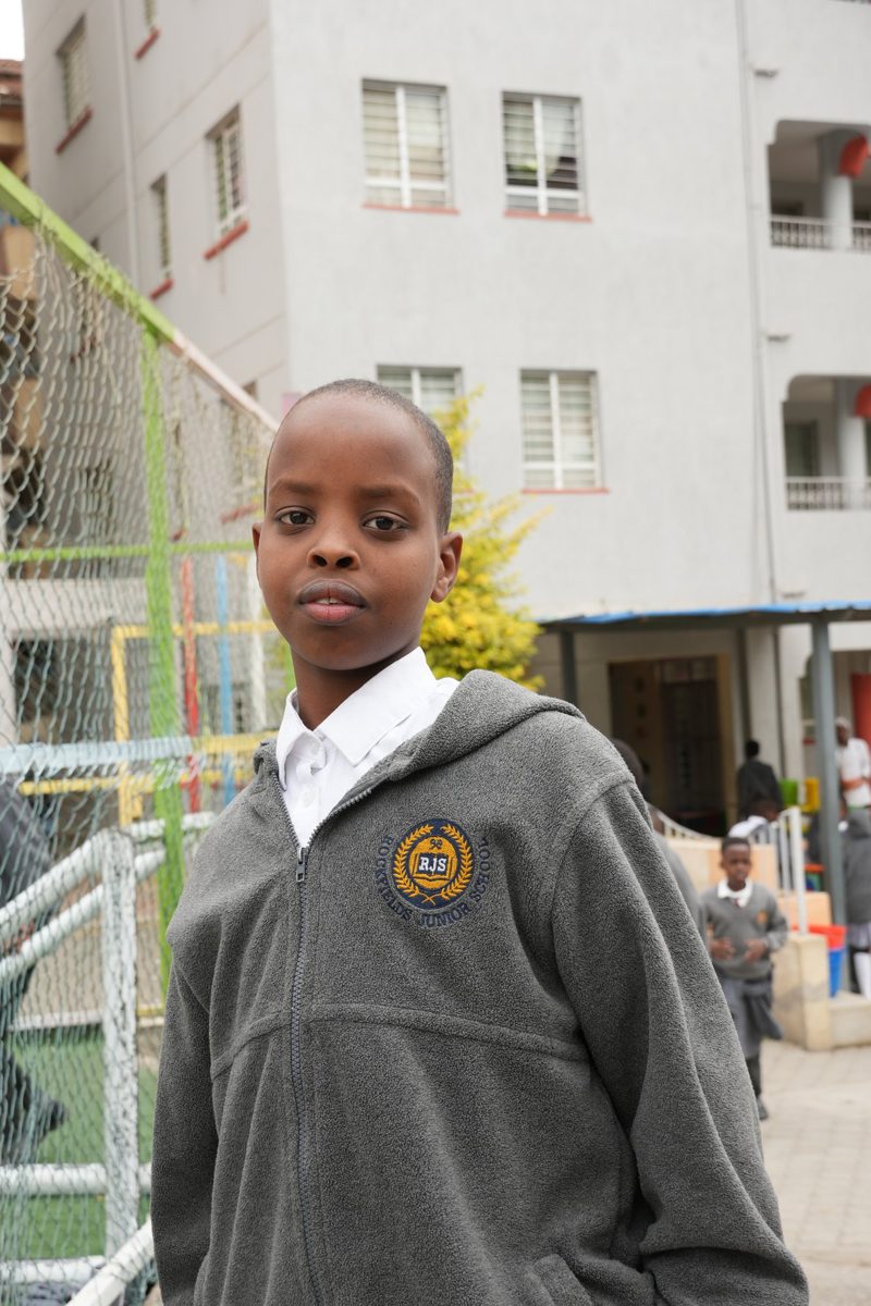 A primary boy in a grey school fleece beside the pitch fence