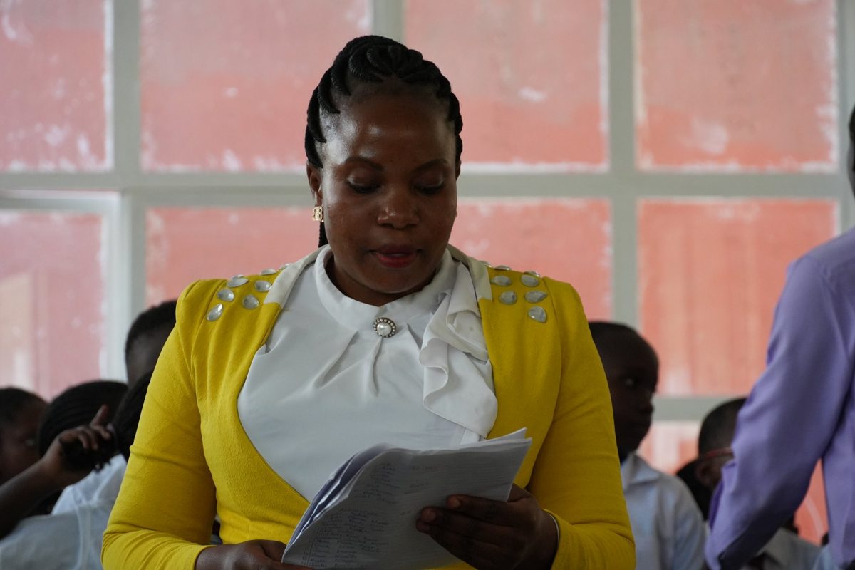 A teacher in a yellow cardigan reading to her class